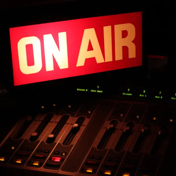 A red sign that says on air next to an audio mixer.